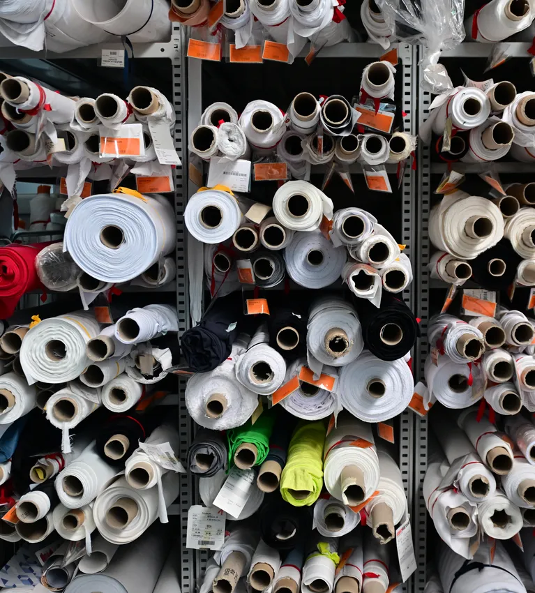 Des étagères remplies de rouleaux de tissu de différentes couleurs et tailles, stockés pour la fabrication de vêtements de sport sur mesure.