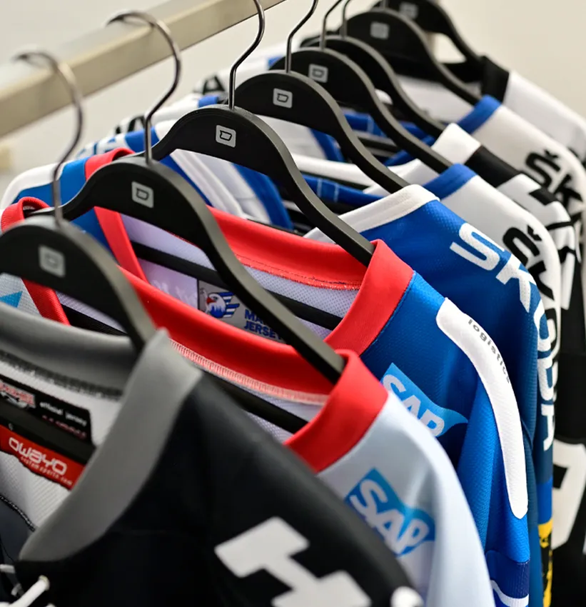 Une rangée de maillots de sport colorés personnalisés de la marque owayo est suspendue sur des cintres noirs sur un portant.