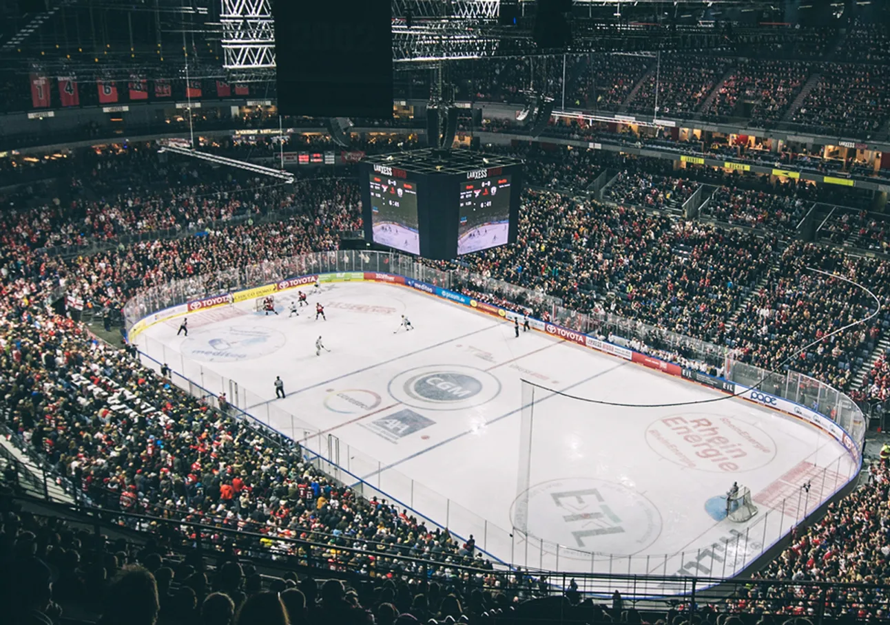 Vue large d'une patinoire pendant un match de hockey avec une grande foule.
