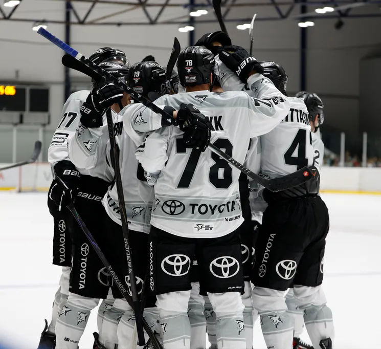 Joueurs de hockey sur glace en maillots blancs avec des numéros noirs et le logo Toyota célébrant sur la glace.