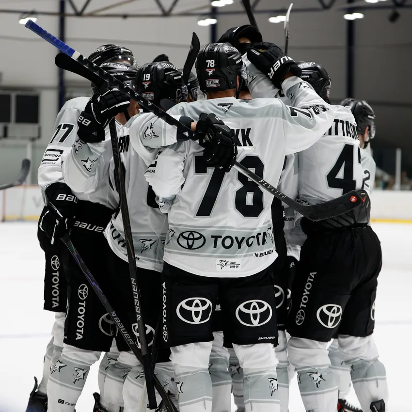 Un groupe de joueurs de hockey sur glace en maillots blancs et noirs s'enlaçant sur la glace.