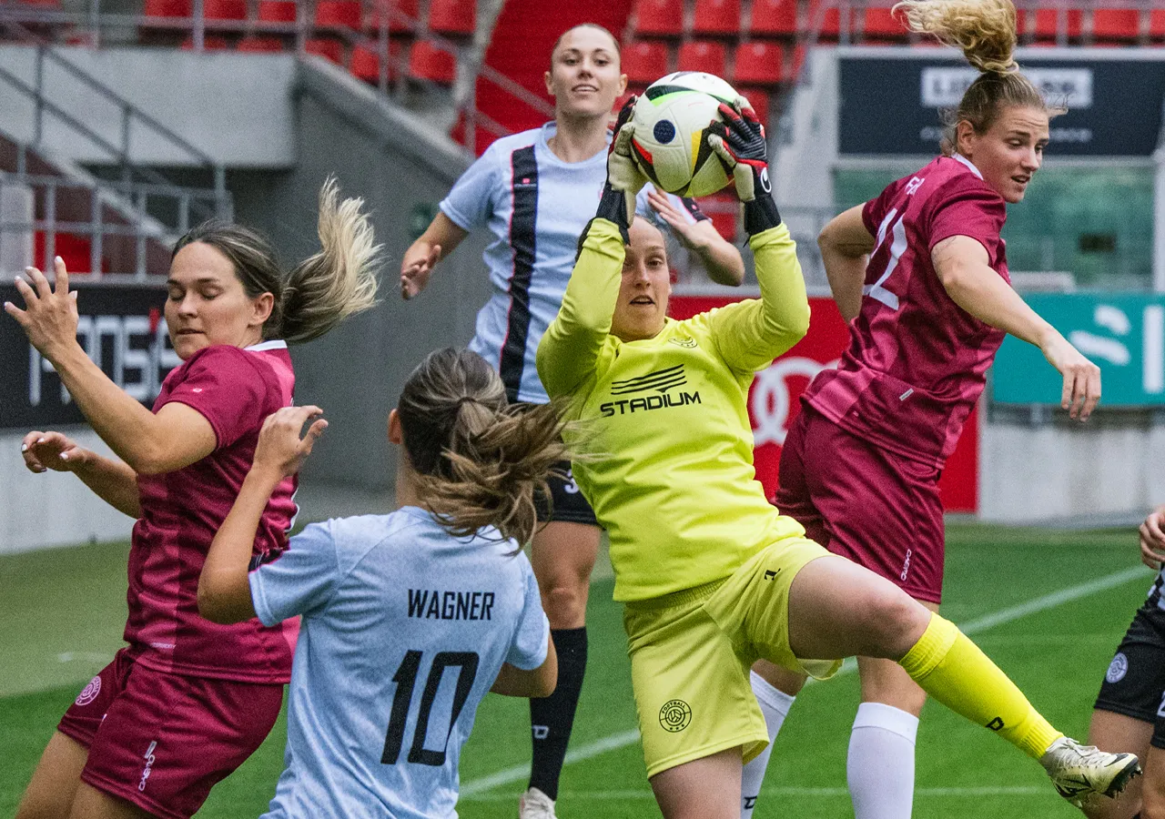Une gardienne de but en tenue de sport jaune attrape le ballon tandis que des joueuses en différents maillots s'engagent autour d'elle.