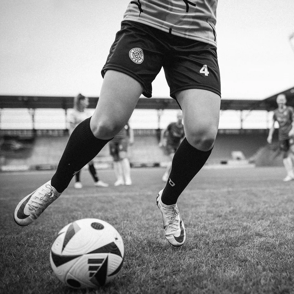 Une joueuse en shorts et chaussettes dribble un ballon de football sur un terrain en herbe.