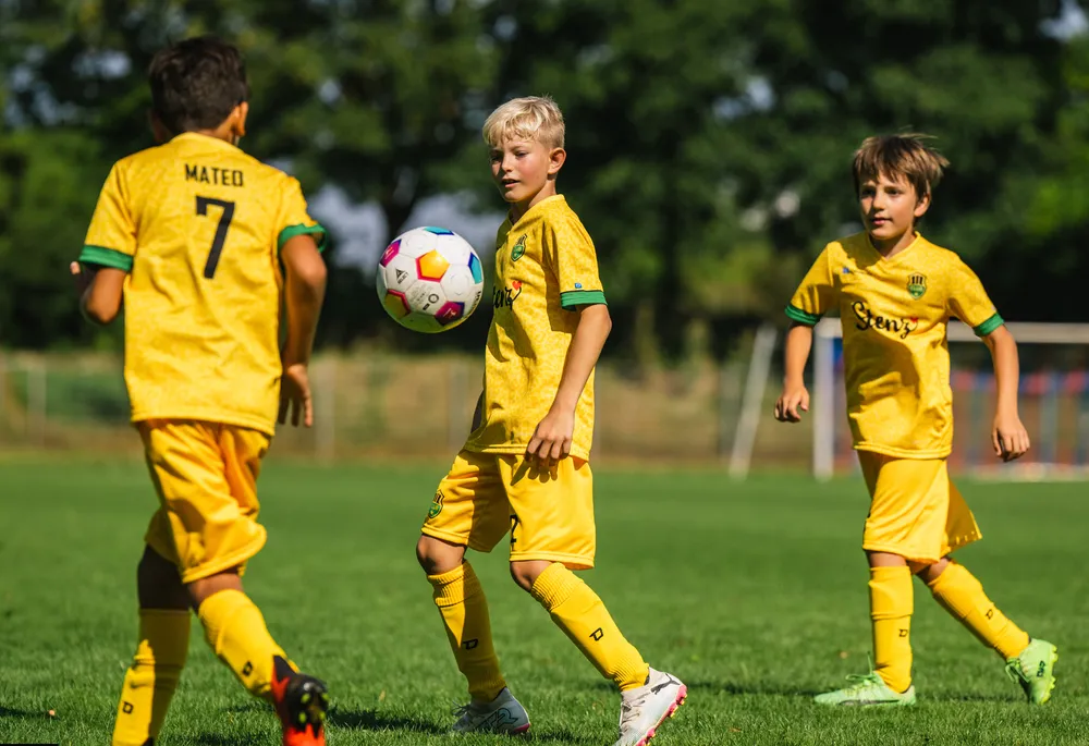 Trois enfants en maillots de football jaunes brillants jouent sur un terrain gazonné.