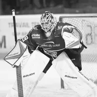 Un gardien de but de hockey sur glace en équipement complet, incluant casque, masque, gants et jambières, est en position de défense sur la glace.