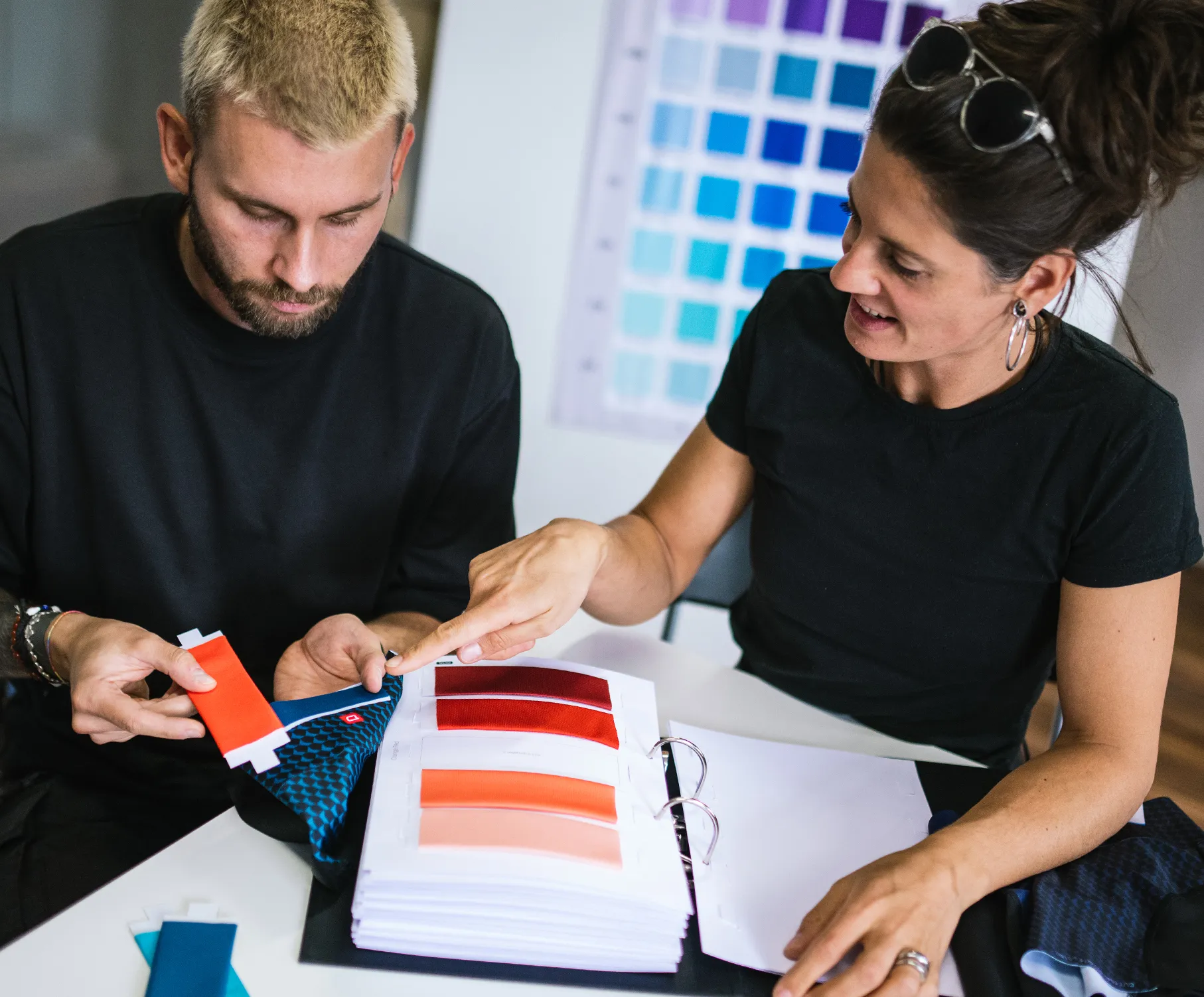 Un homme et une femme choisissent des couleurs pour des vêtements de sport sur mesure, en examinant des échantillons de tissus et des nuanciers.