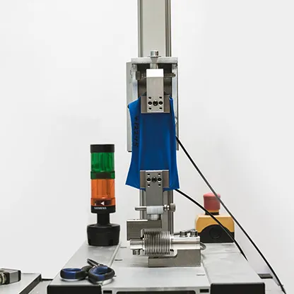 Un tissu bleu est testé dans une machine sur une table de travail, à côté d'un voyant lumineux et d'outils.