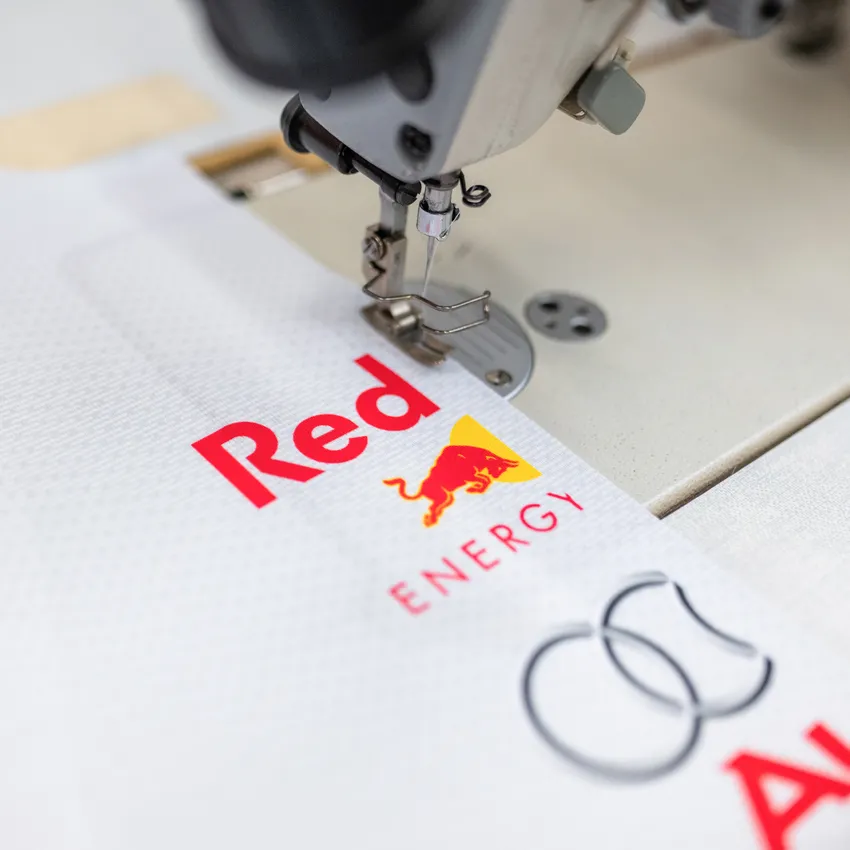 Une machine à coudre qui coud sur un tissu blanc avec des logos colorés.