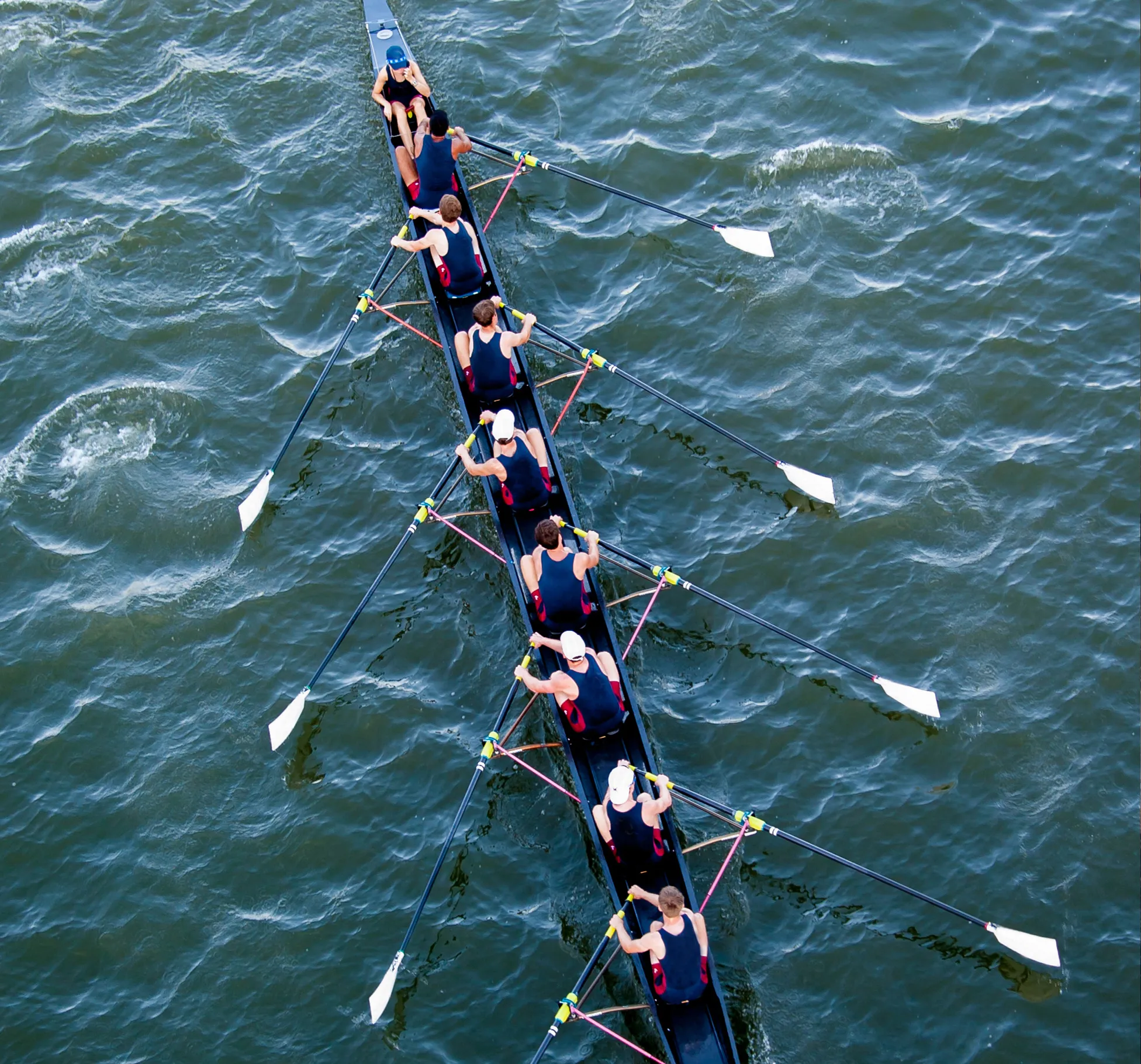 Un groupe de rameurs en vêtements de sport assortis rame en synchronisation sur un plan d'eau.