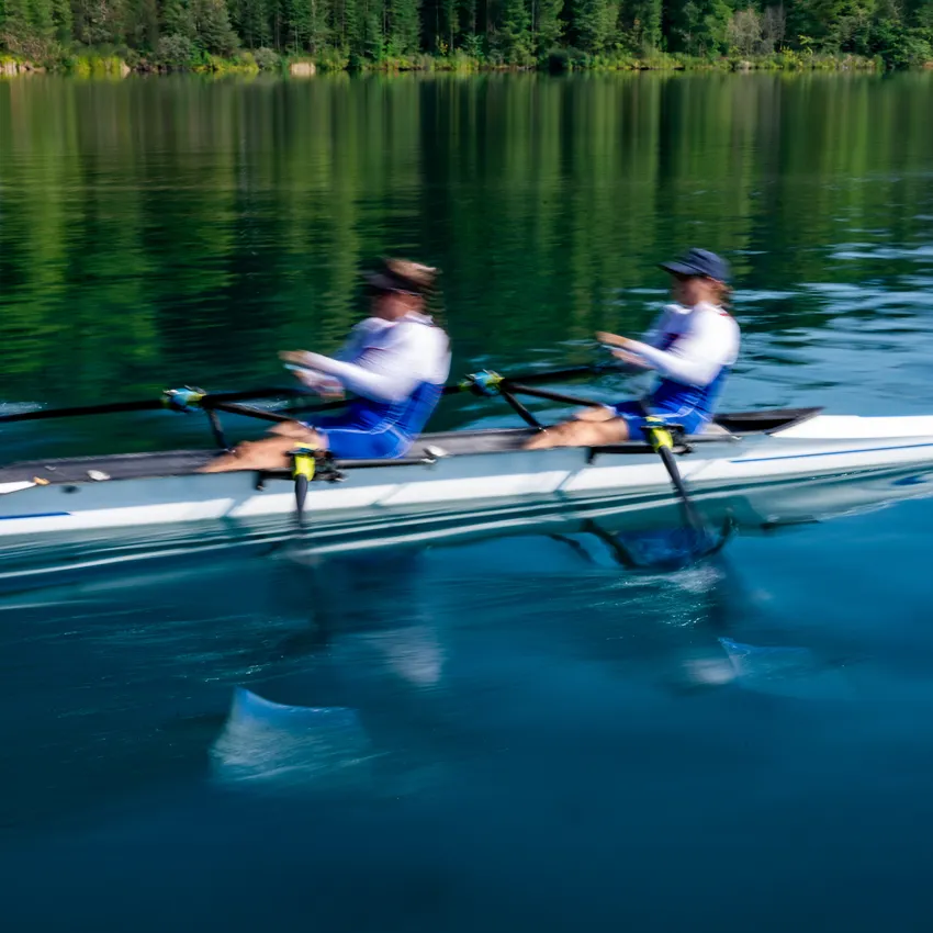 Deux rameurs en vêtements de sport bleus effectuant des coups puissants sur un lac calme.