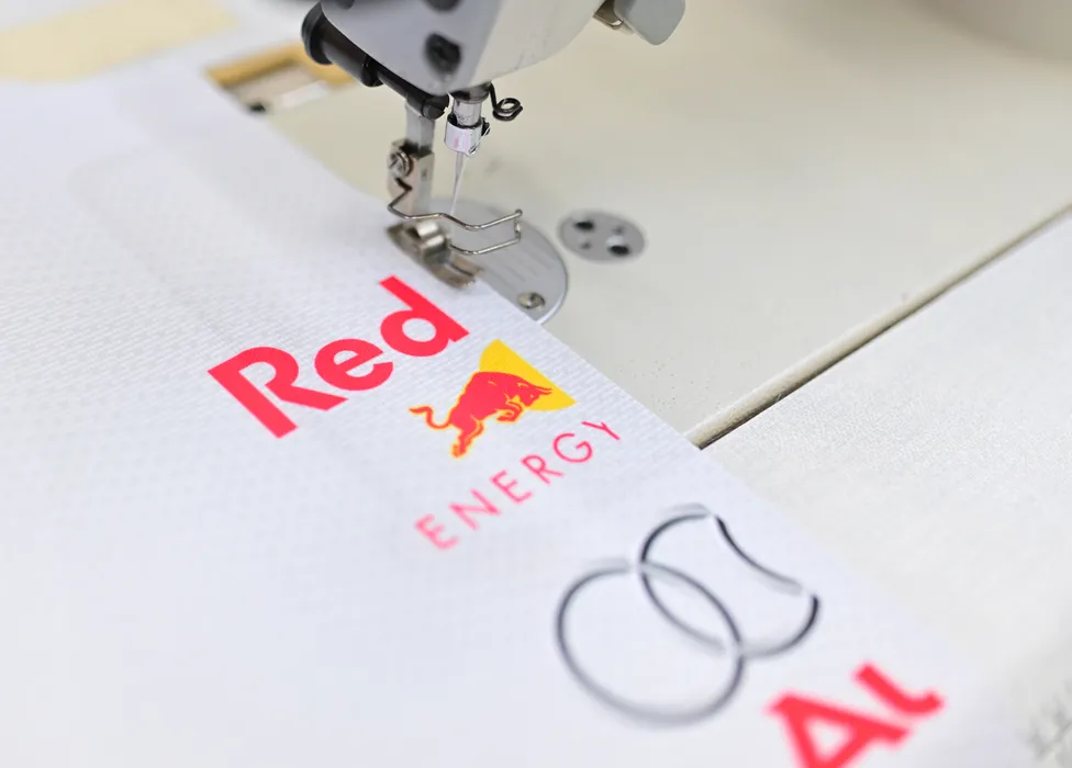 Une machine à coudre brode un vêtement de sport blanc avec le logo rouge Red Bull Energy et un autre logo.